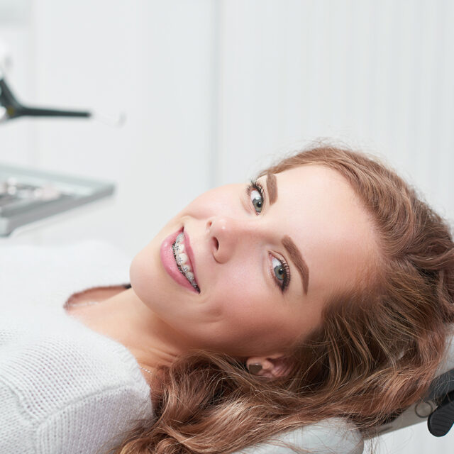 Happy young ginger haired woman with braces smiling to the camera sitting in a dental chair at the clinic waiting for examination copyspace positivity healthcare medicine dentistry people smile.